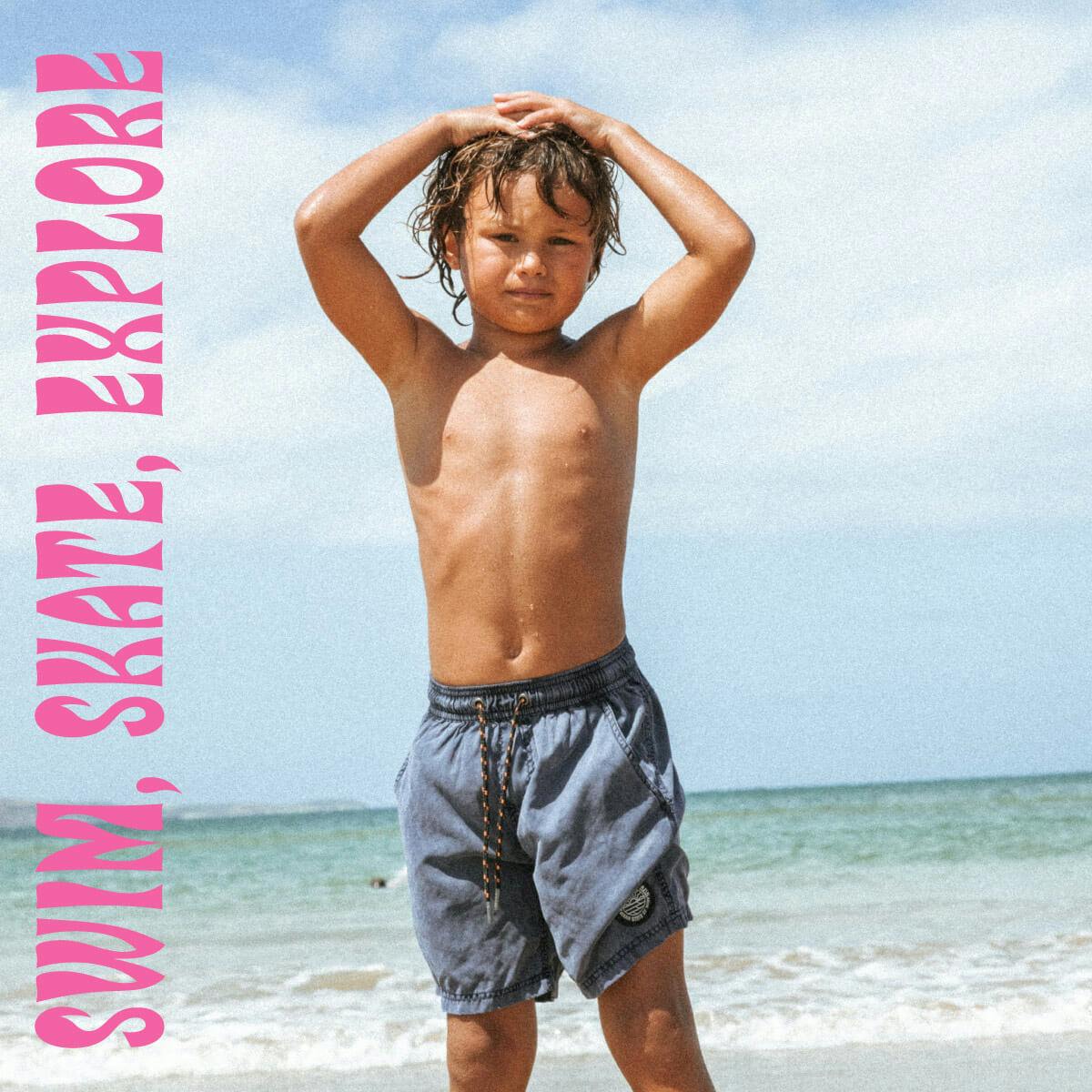 Young boy stands at the beach in the Everyday Shorts with his hands on his head. 