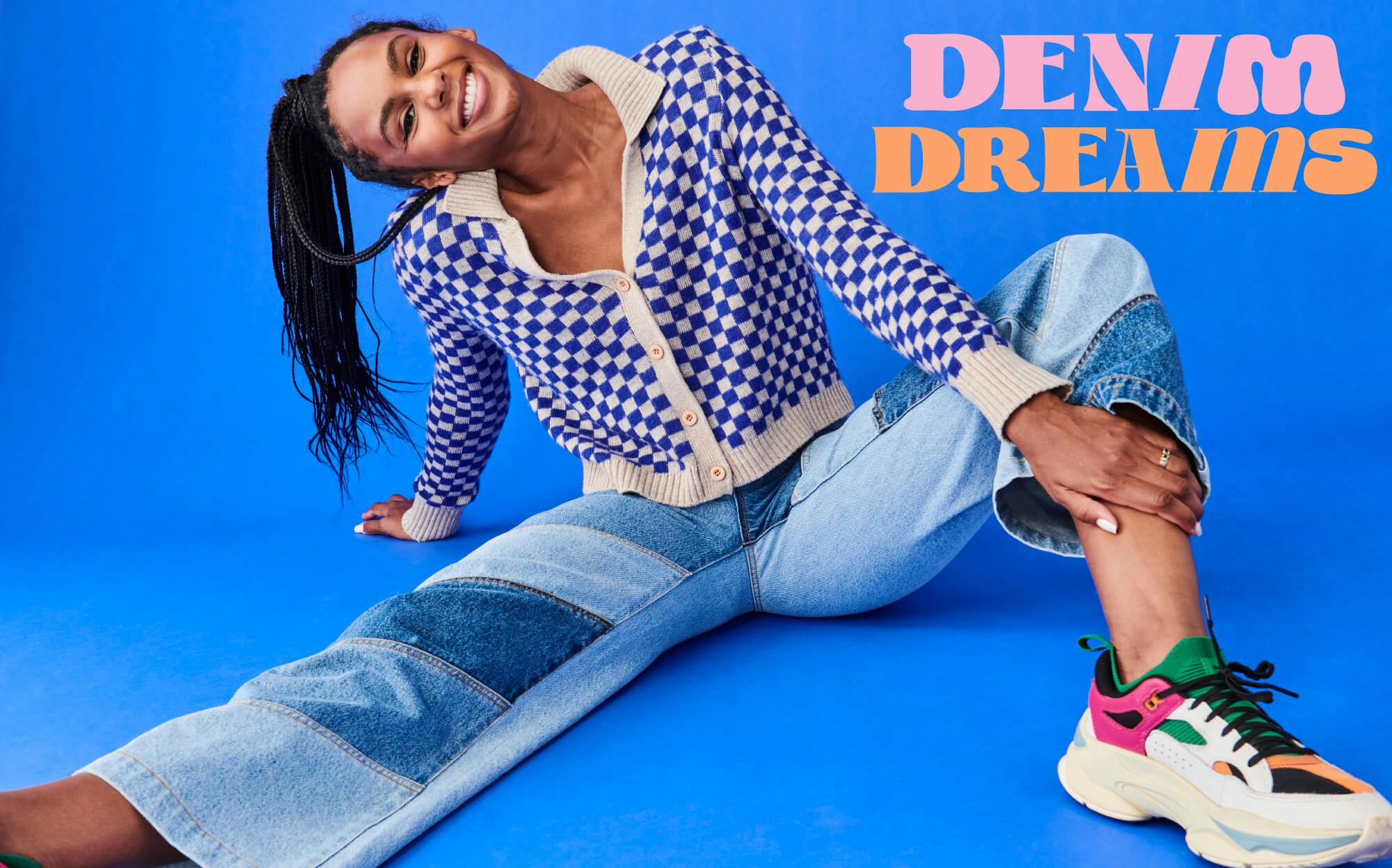 Female model sits on floor with blue background behind her, she wears the Cameron Jeans in Diagonal Patchwork and the Race Cardi in Electric Blue Check. Text overlay: Denim Dreams