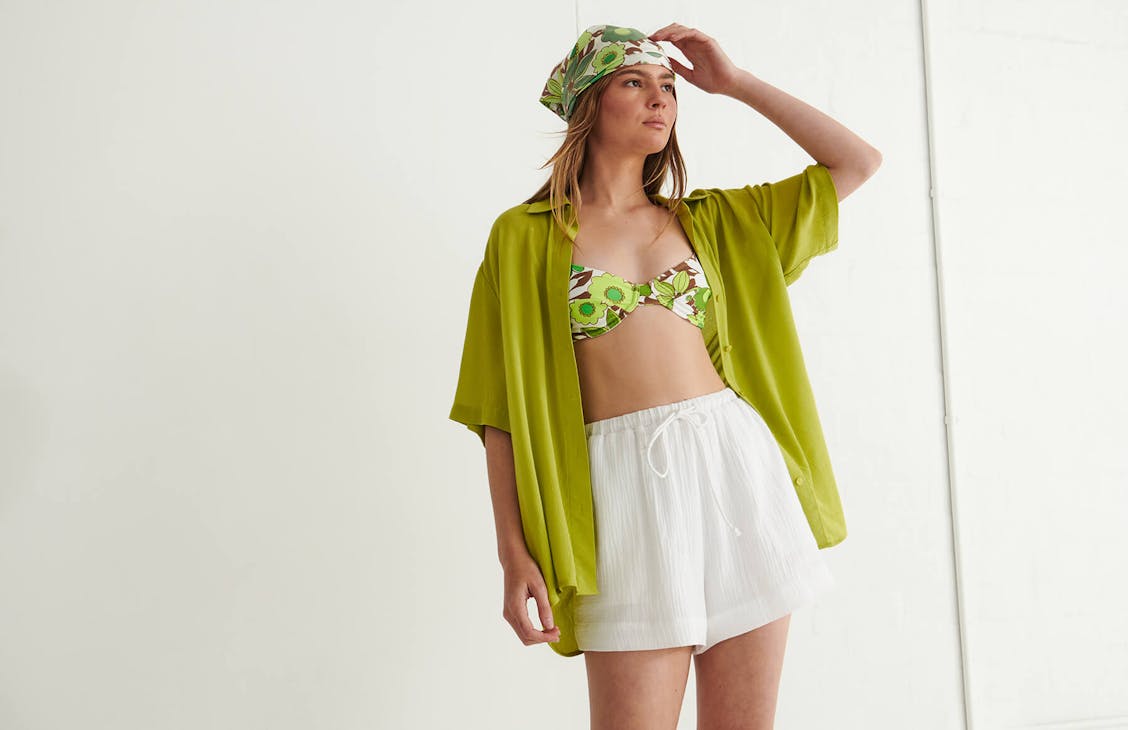 Female model wearing the Marcie Shorts in White with a green shirt over bathers.