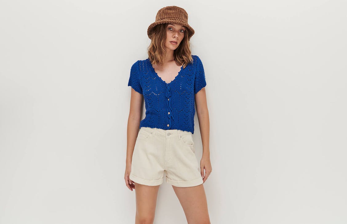Model wears the Holly Cord Shorts in cream with the Betty Crochet Top in blue with the Mini Bucket Hat in Mud