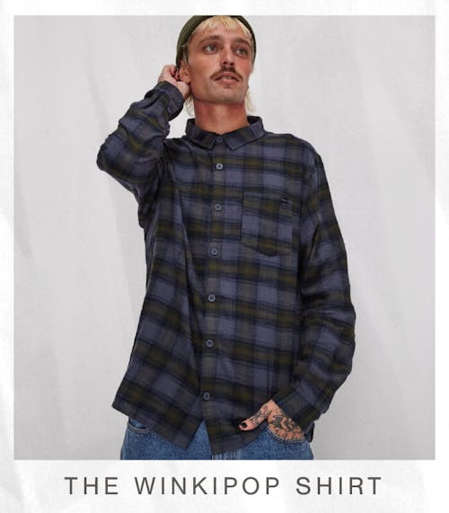 Image of male model in studio, with one hand resting begind his head and the other hand in his pant pocket. He is wearing the Winkipop Shirt; Moss Check . Text reads 'The Winkipop Shirt'.