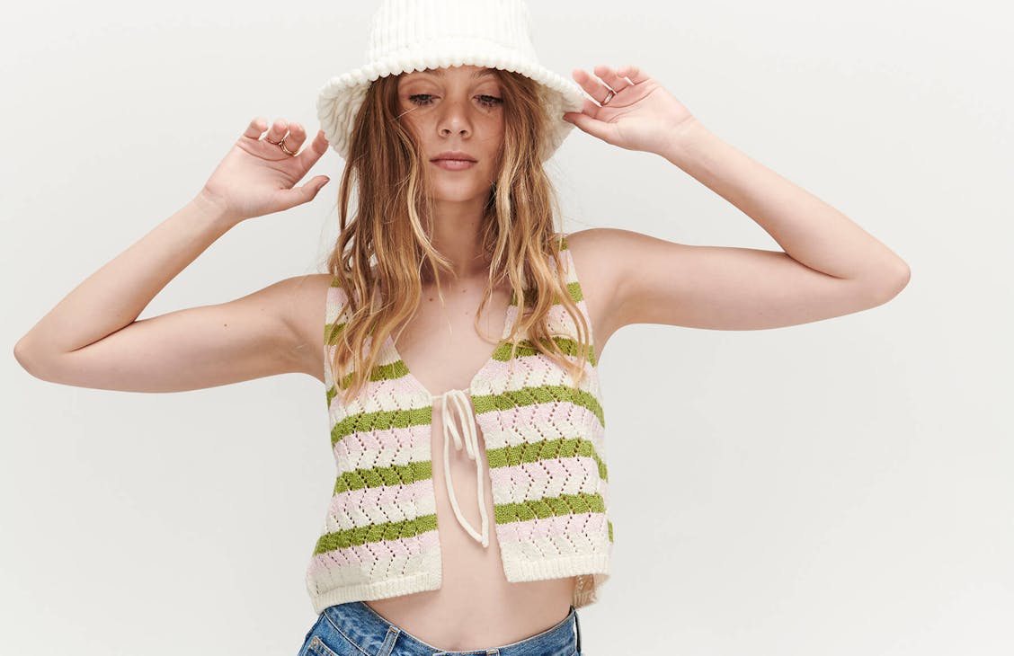 Female model wearing the Fiesta Crochet Top in Fiesta Stripe, grabbing onto her bucket hat.