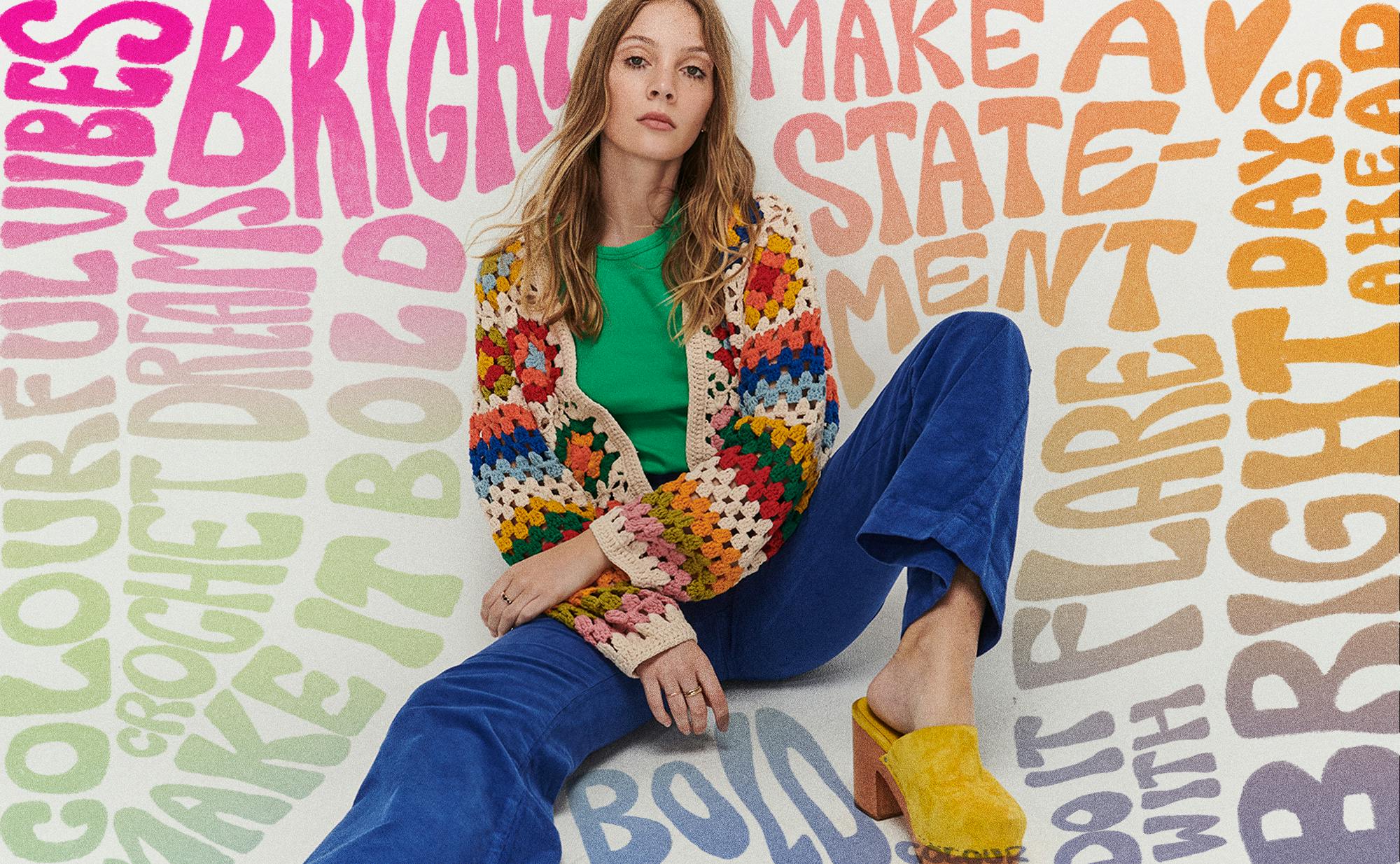Female model wearing the prismatic cardi and cord flares in baddie blue sits slouched amongst colourful wording.