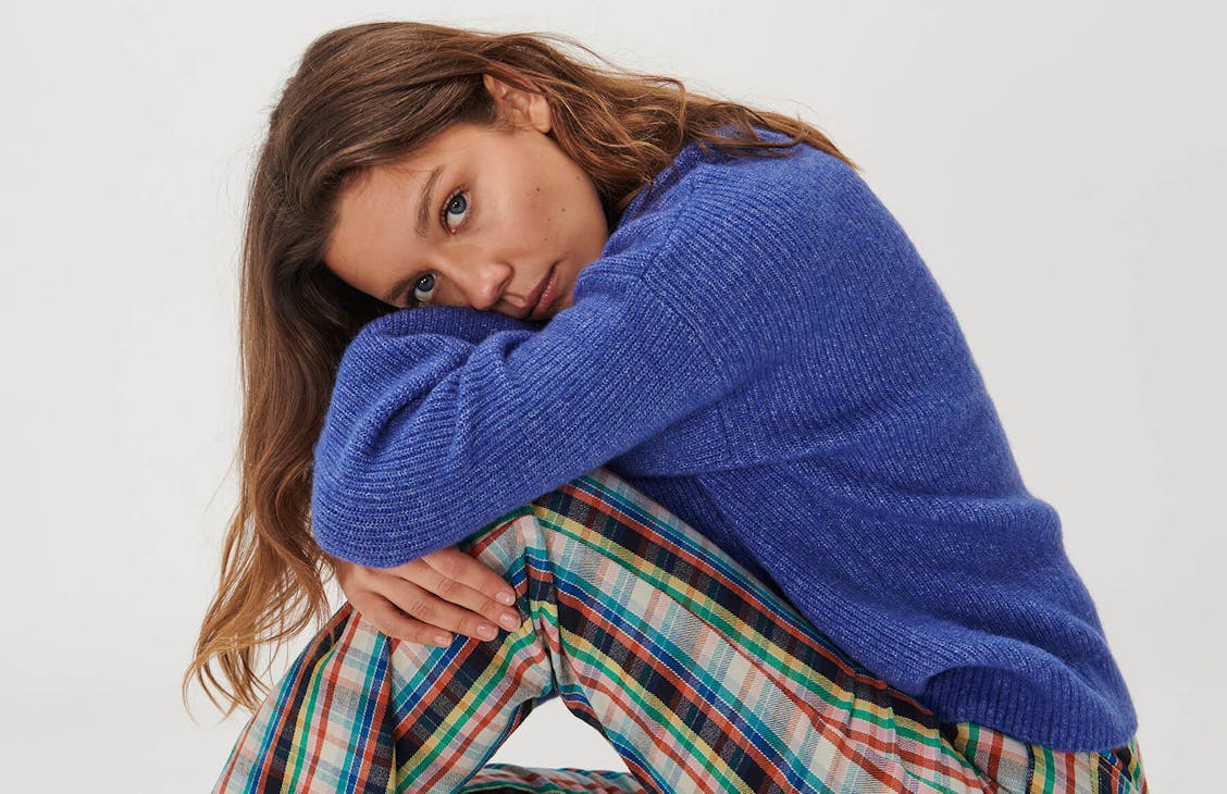 Image of model in studio wearing the Brady flares and Everly knit in blue. She is sitting down hugging her knee