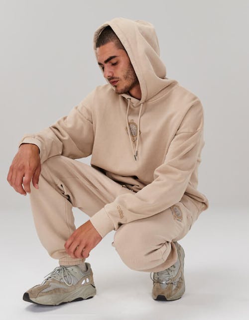 Image of male in studio. He is wearing the Slouched Hoodie and Crew in Soy and is squatting down. 