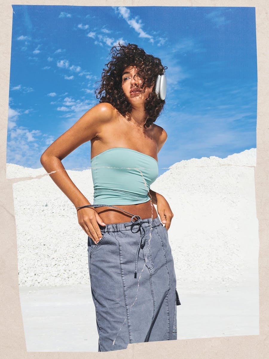 Image of female model wearing grey cargo maxi skirt and a blue boob tube, blue skies and white sand behind her. 