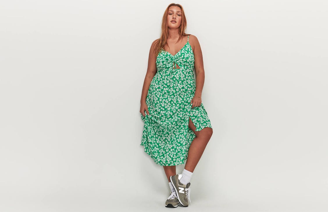 Image of female in studio wearing a green floral midi dress with sneakers. 