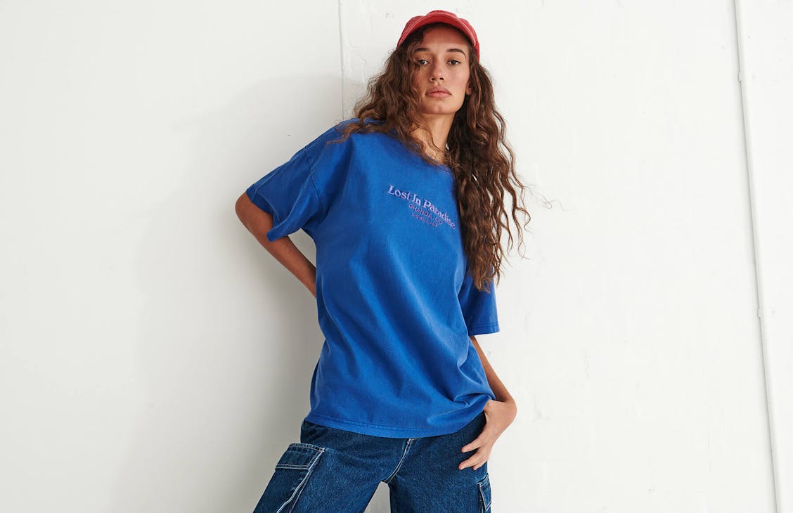Model poses in studio in Blue T-shirt, red hat and jeans.