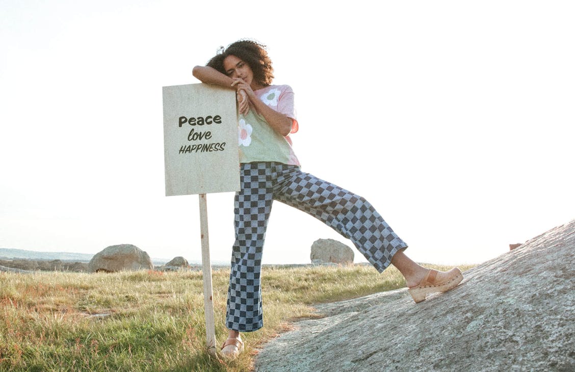 Female model wearing the Cameron Jeans in Denim Checkerboard standing on a rock, leading on a protest sign.