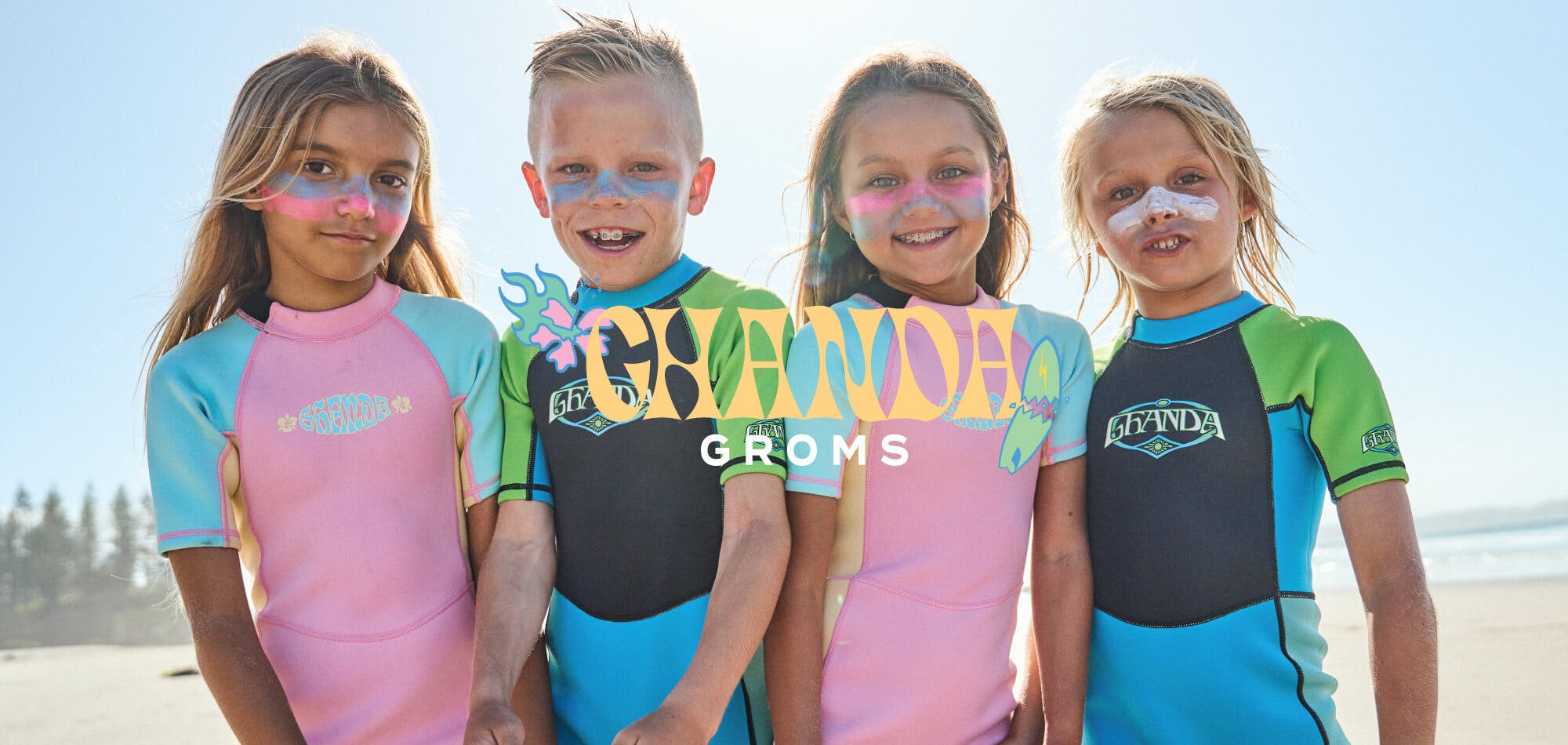 Two boys and two girls wearing ghanda wetsuits at the beach with colourful zinc on there faces