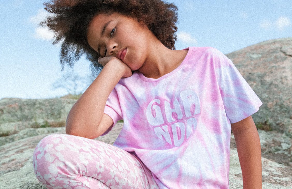 Young female model wearing the bibs tee in Lollipop Tie Dye with the beach bell flares in pink carmen floral.