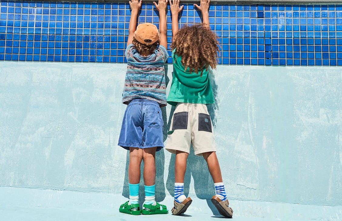 Two young boys hanging off the side of an empty pool, backs to camera.