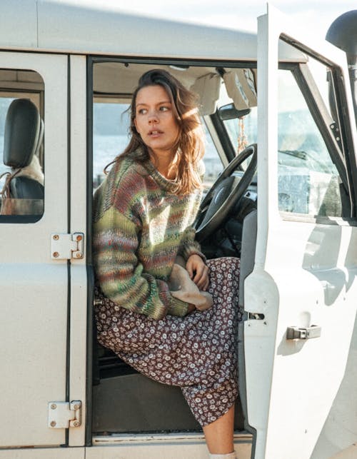 Image of female sitting inside the car with the door open. She is wearing the Emile Skirt in Brown Addison Floral and the Oslo Knit in Green Salsa Stripe