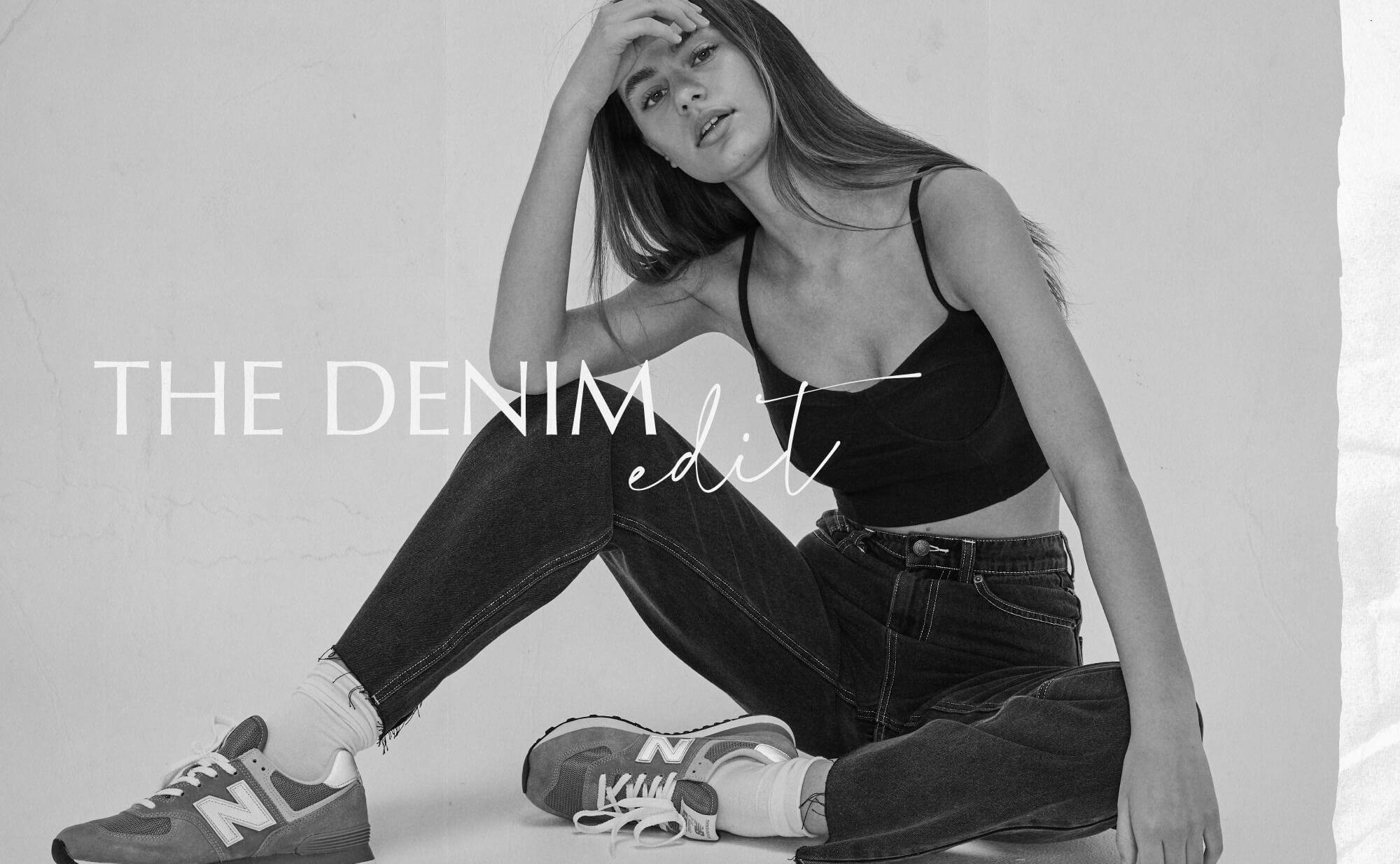 Black and white image of female model sitting in studio. She is wearing the Worker Jeans with a small black crop top. Text reads The Denim Edit. 