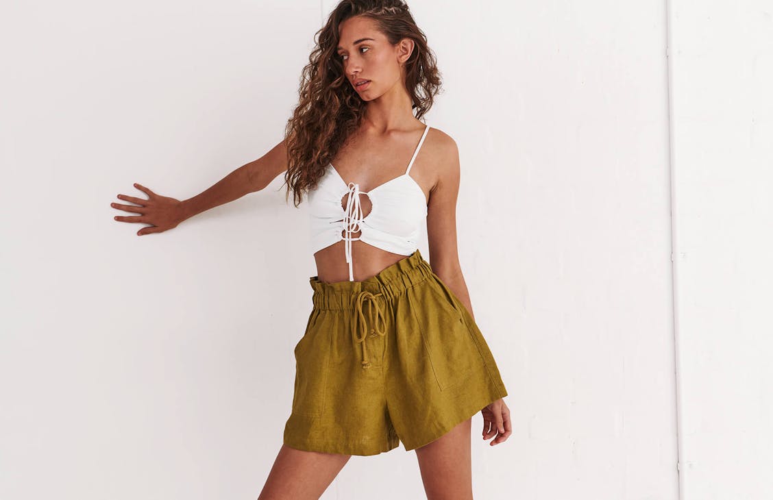 Image of female model in studio, she is wearing olive green linen shorts and a white top with keyhole cutouts