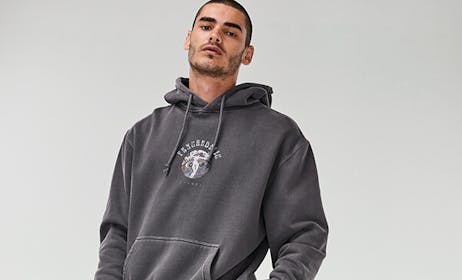 Image of male in studio, he is wearing a grey hoodie with chest print