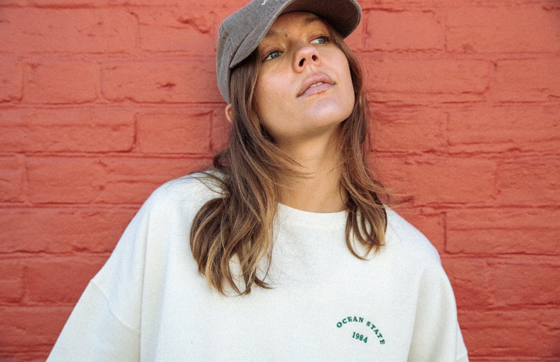 Image of model wearing the cool crew and classic cap, standing infant of a red brick wall. 
