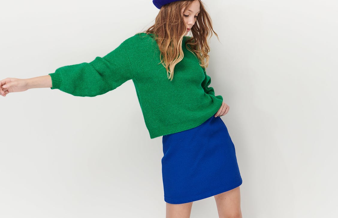 Image of female model in studio, she is wearing the Everly Knit with the College Skirt in Baddie Blue with the Paris Beret.