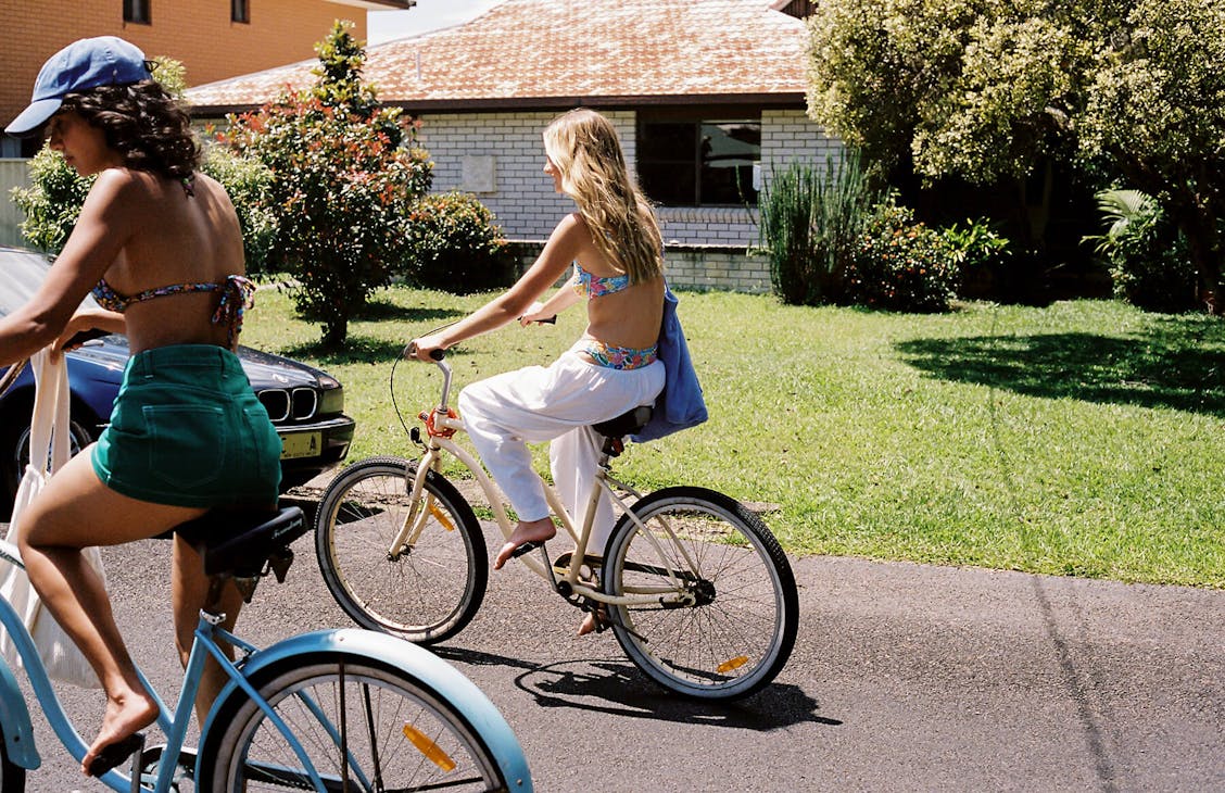 Female model wearing the white Noosa Pants riding a bike on the road.
