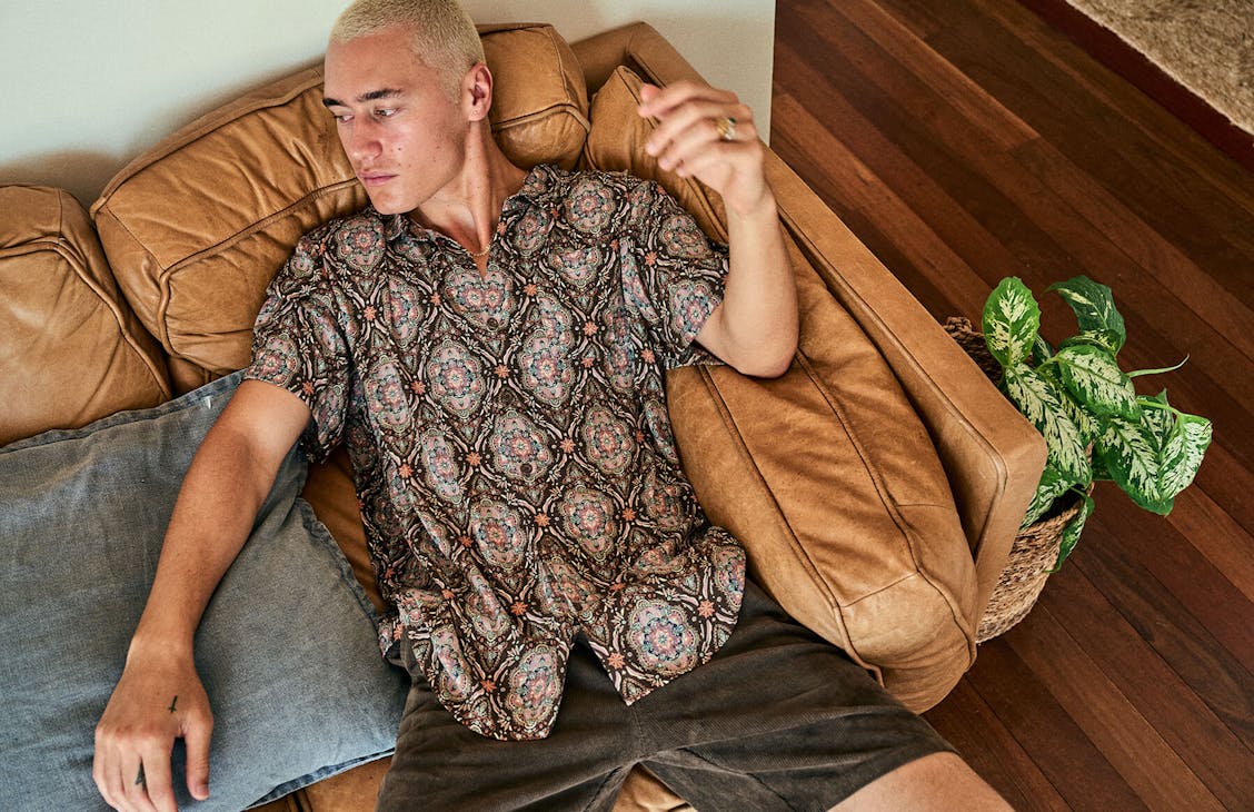 Male model wearing the Shapers Shirt in Kaleidoscopic Brown lounging on a leather couch. 