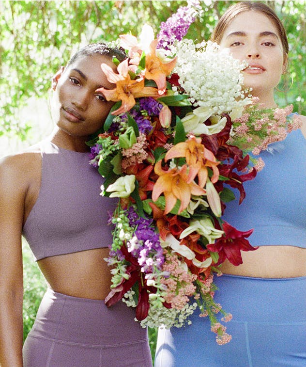 Two models posing in GirlfriendCollective activewear holding flowers. 