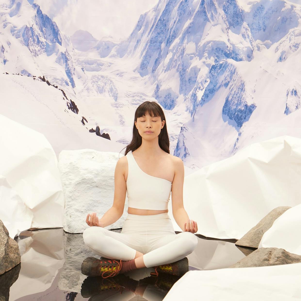 Woman sitting on ice meditating wearing Girlfriend Collective one-shoulder sports bra