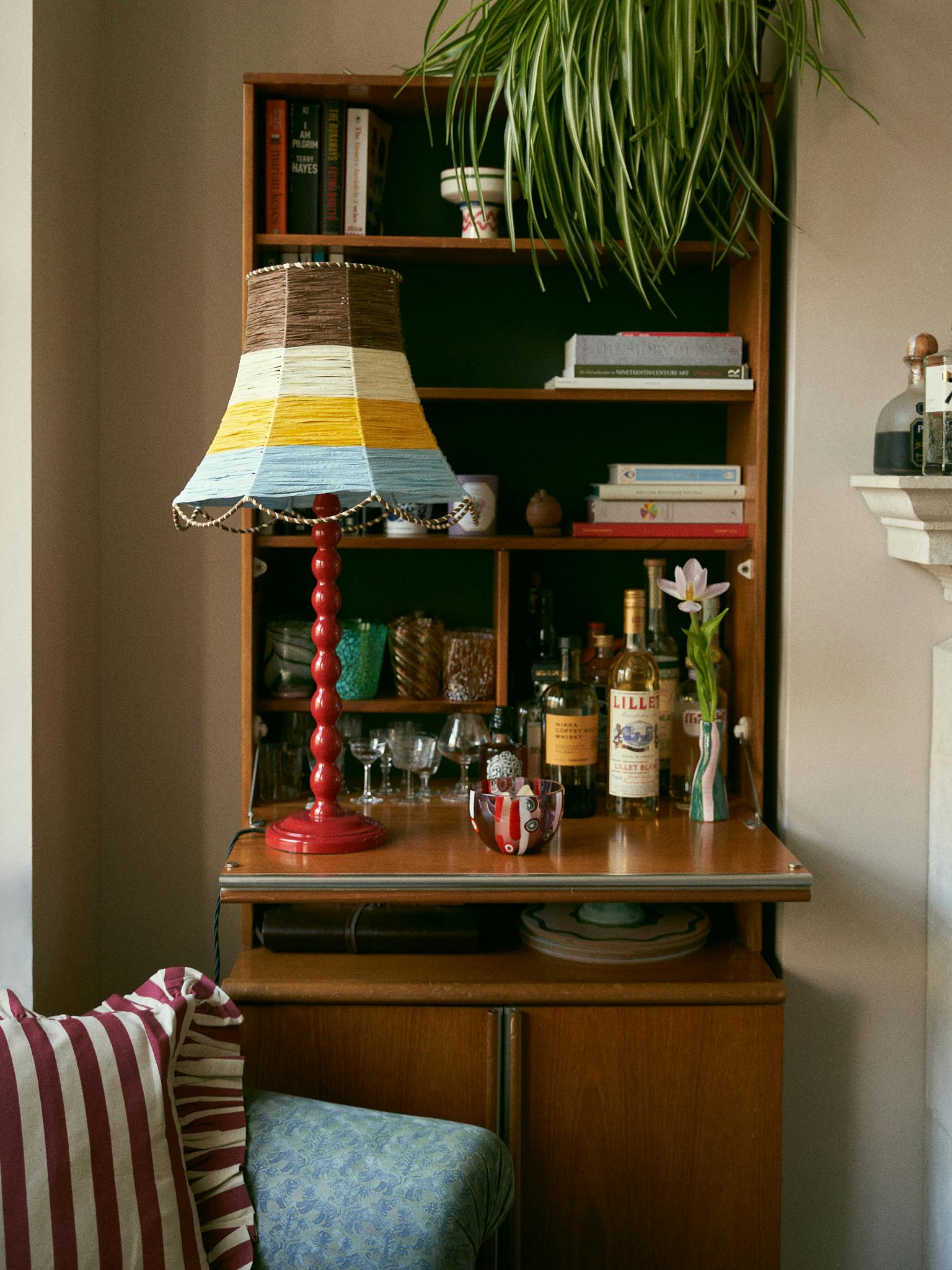 A red bobbin lamp base on a dresser with stripy lampshade