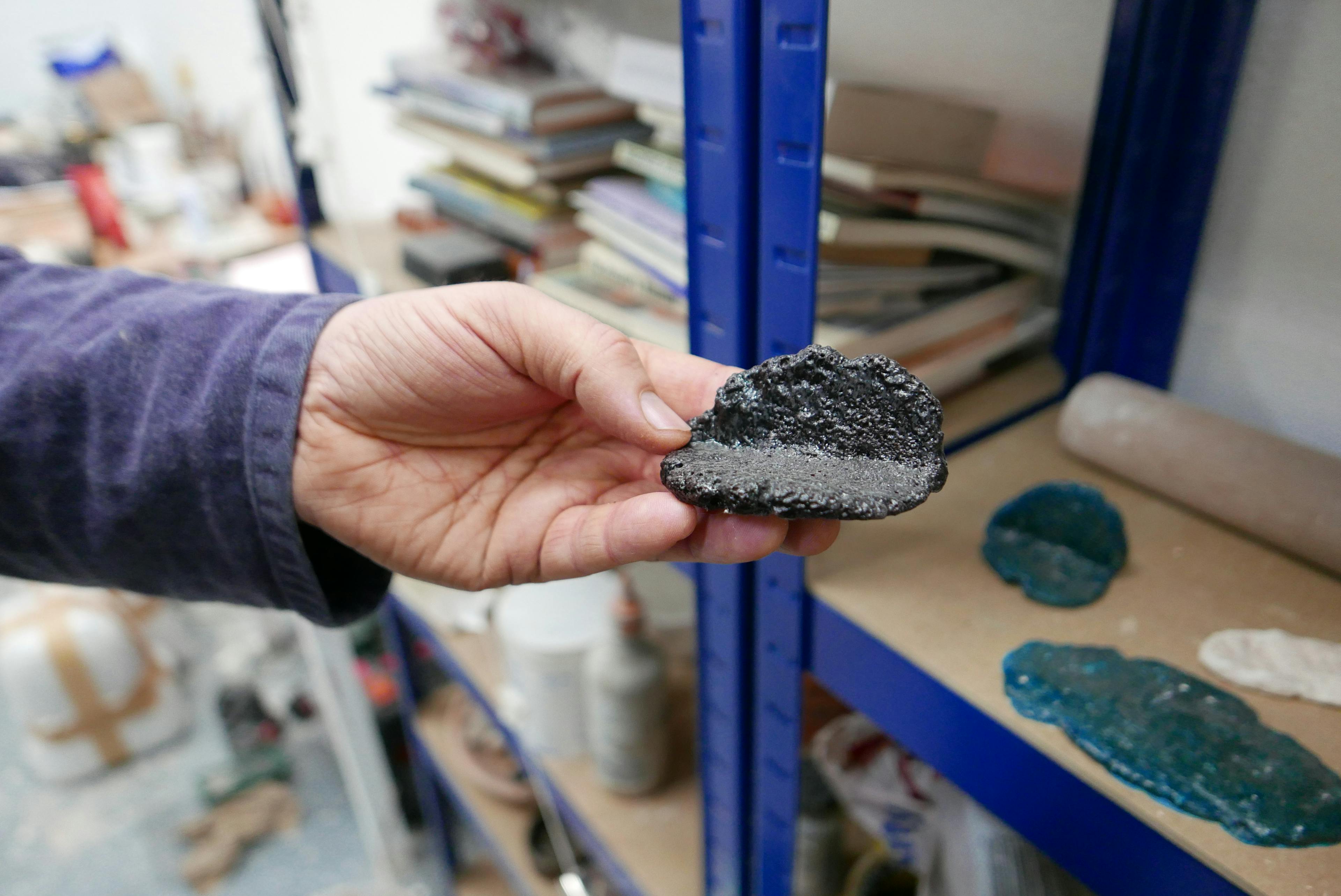 A hand is holding a fired clay specimen in a ceramic studio. 