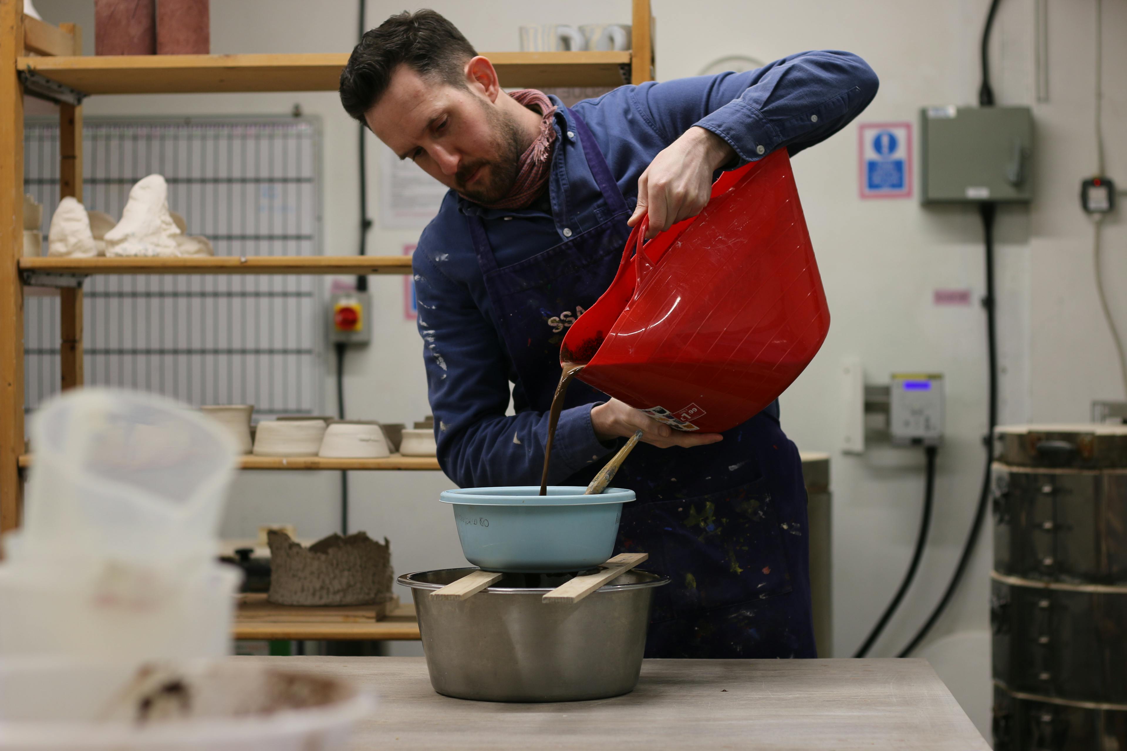 Portrait of a ceramic maker Steven Sales. H eis pouring clay from a bucket into a sieve. 