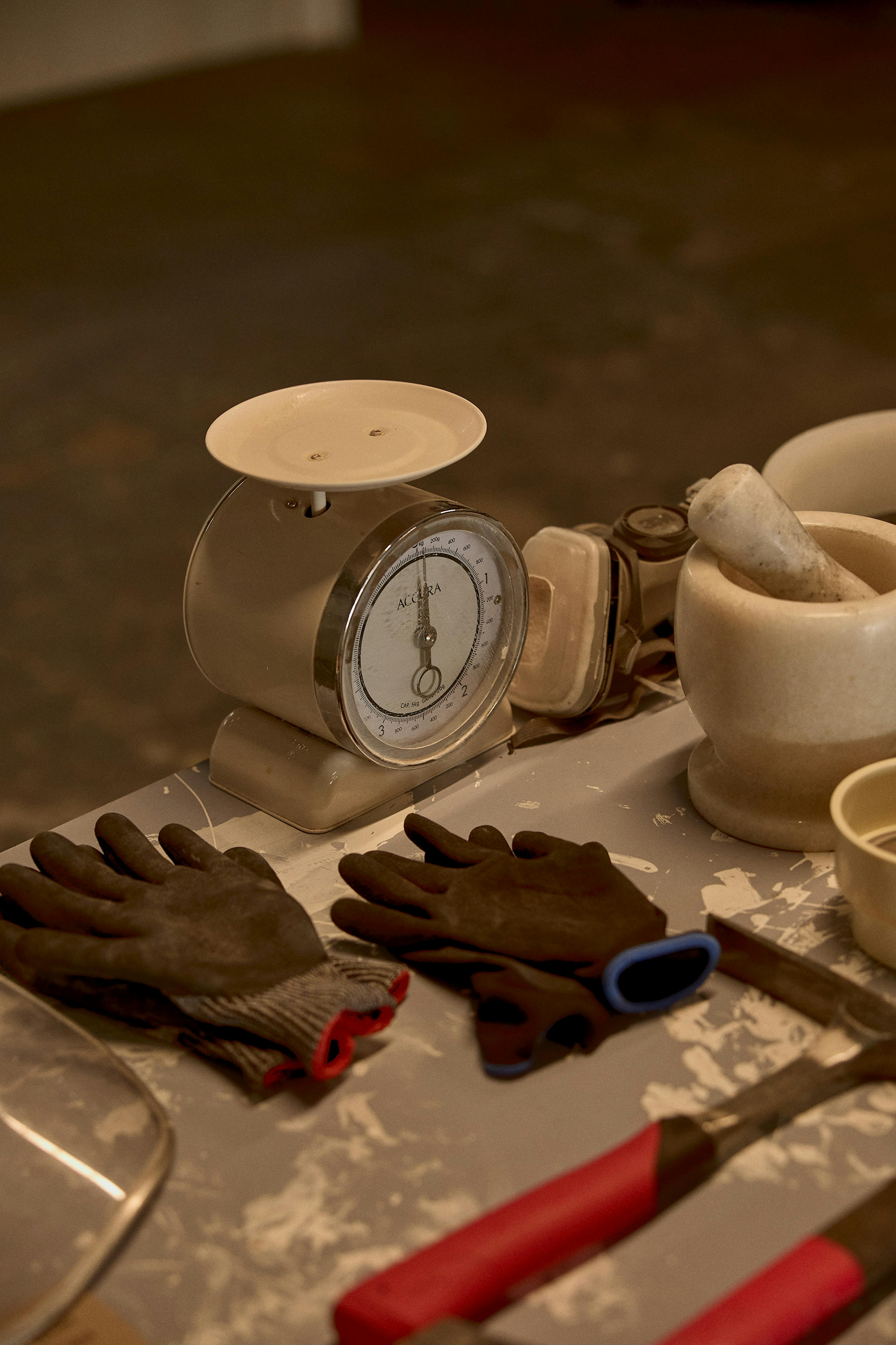 This image shows an old school scales, working gloves and other tools as well as pestle and mortar. 