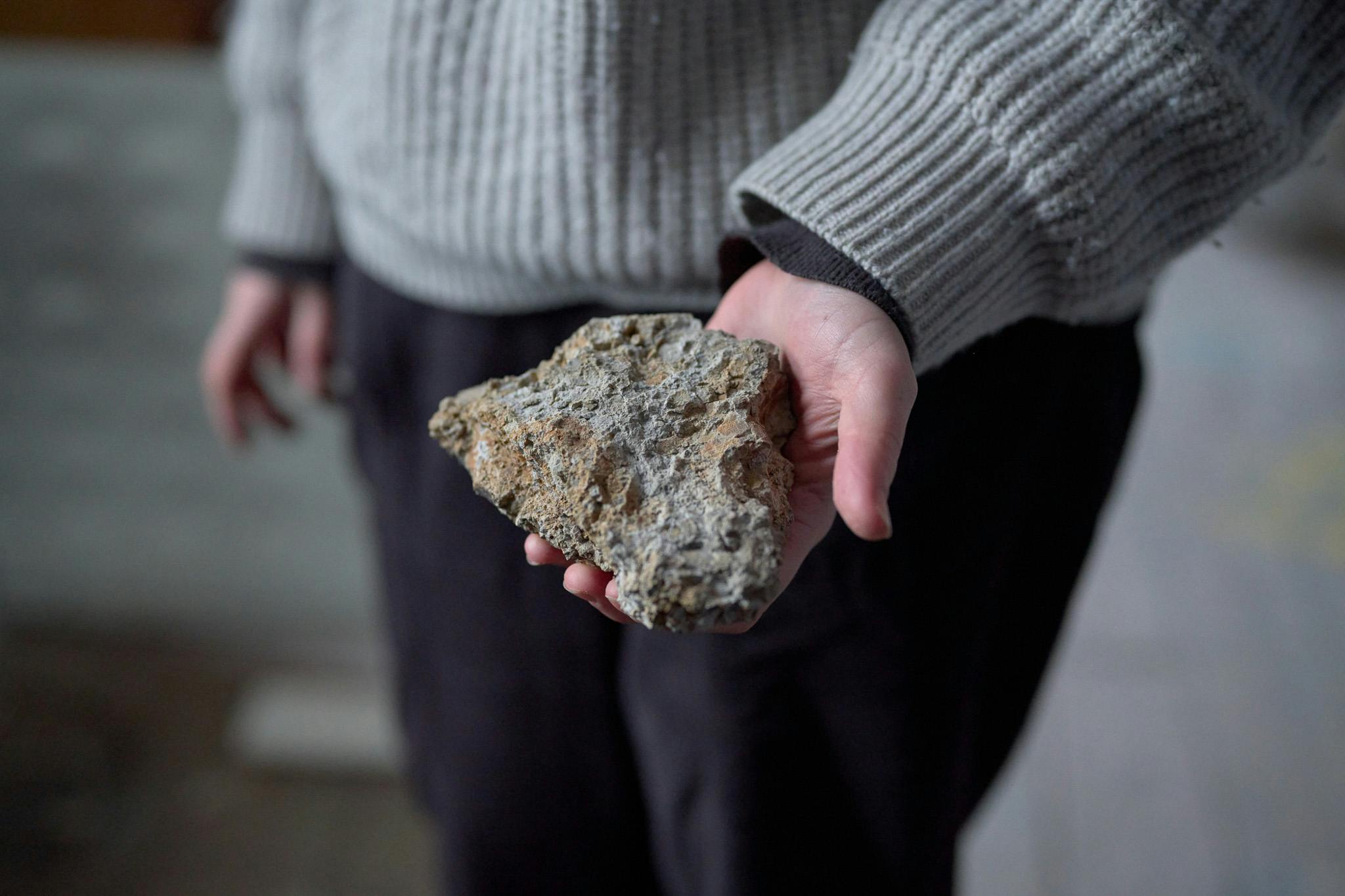 A hand is holding a grey and textured rock like piece of clay.