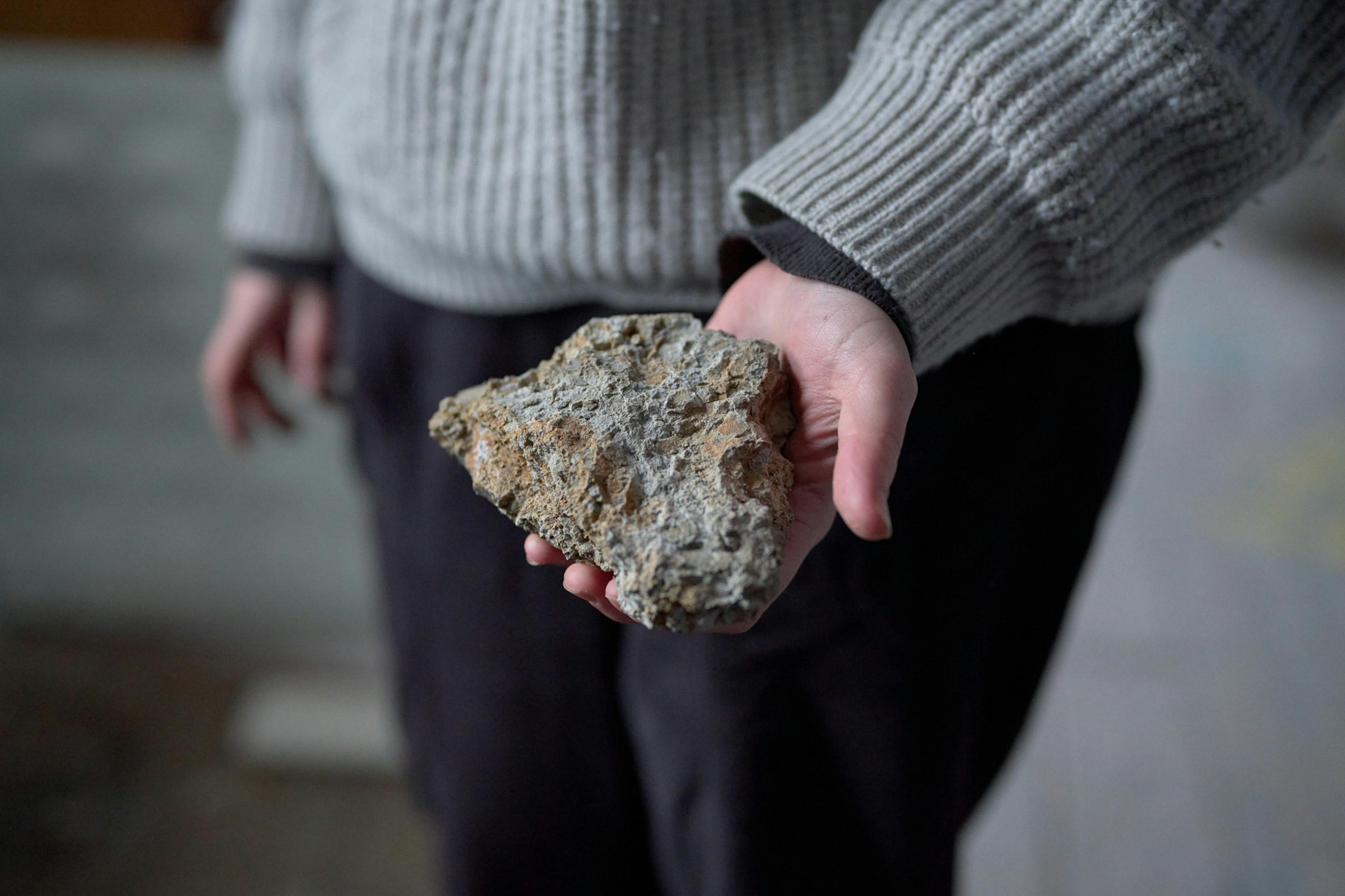 A hand is holding a grey and textured rock like piece of clay. 