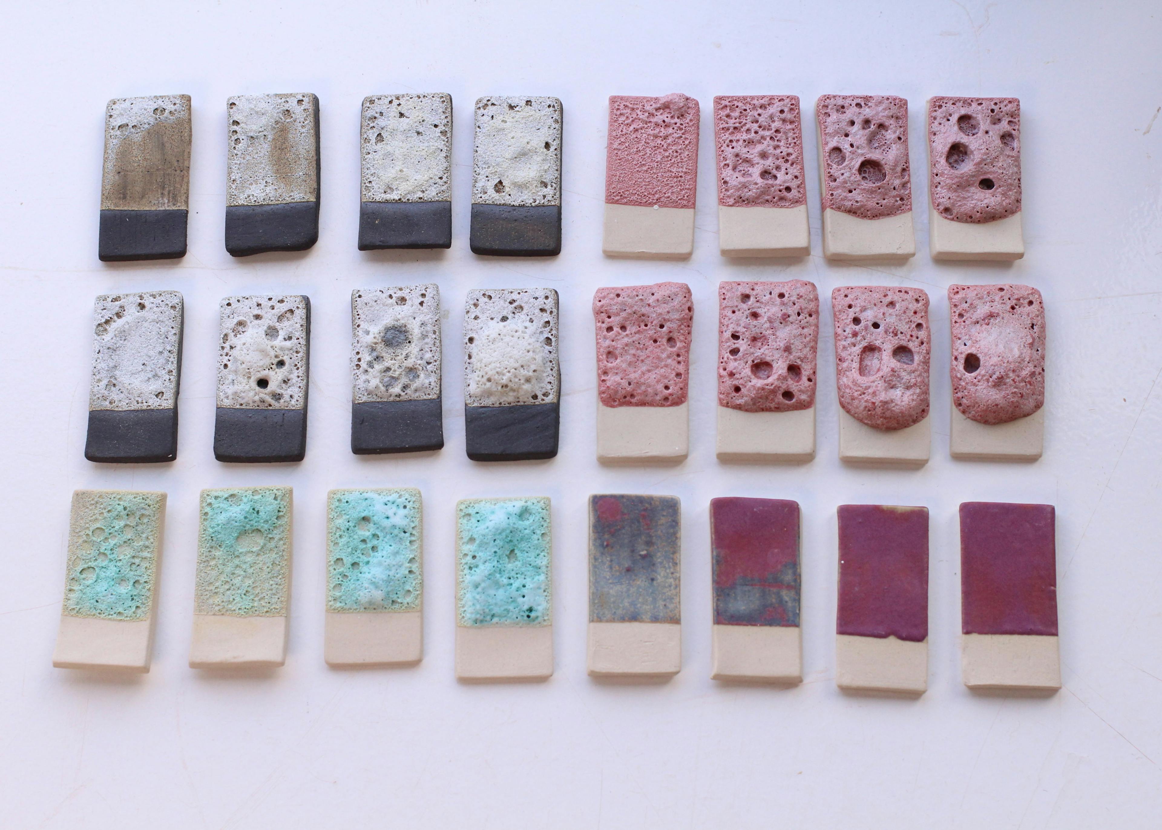 An image of ceramic glaze test tiles lined in 3 rows. The tiles showcase lava glazes in pink, white and turquoise colour. These glazes are very textured and remind one of lychen. 