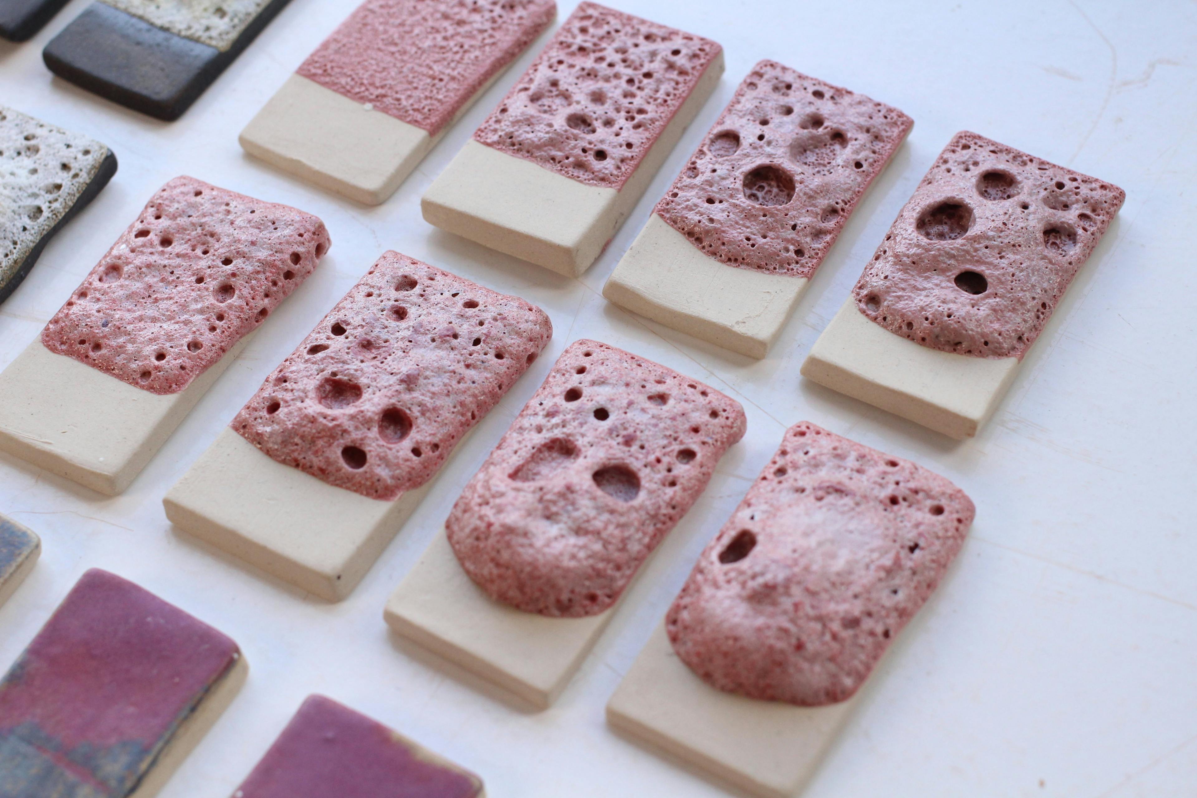 An image of ceramic glaze test tiles lined in 3 rows. The tiles showcase lava glazes in pink, white and turquoise colour. These glazes are very textured and remind one of lychen. 