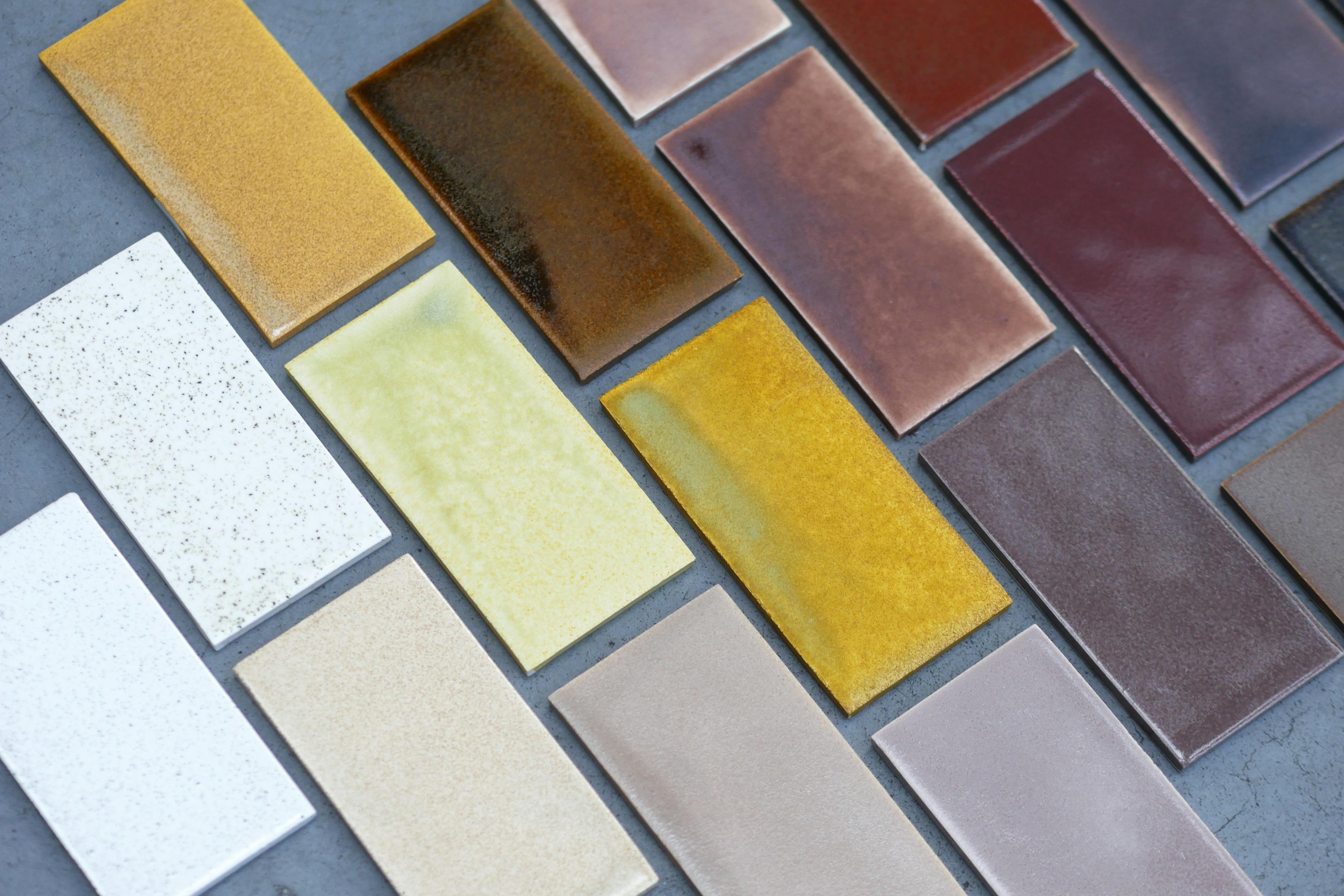 This image shows multitude of raws of ceramic glaze test tiles. They gradate from light grey, through ochre and brown into dark maroon and black. Waste material has been used to cretae this pallet of pottery glazes. 