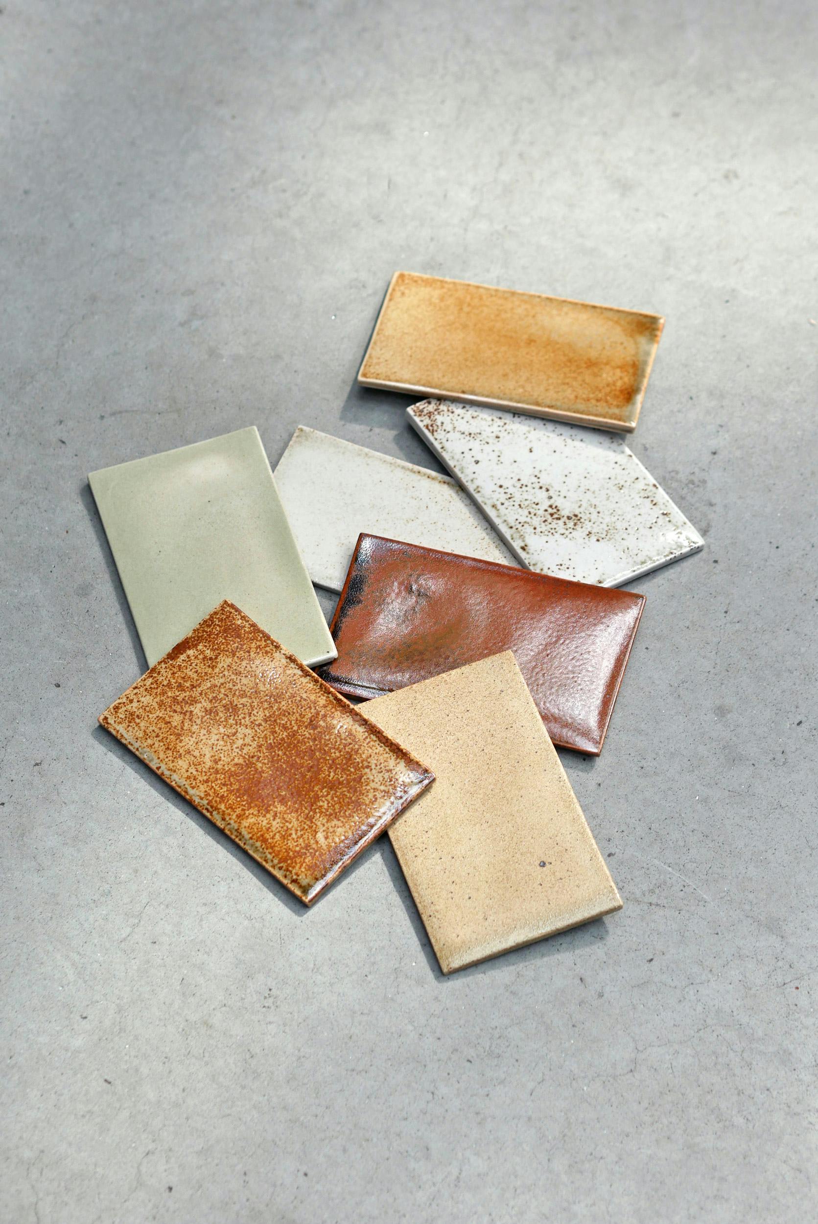 Artistically scattered rectangular ceramic tiles on a grey background. They are warm in tone and are ochre to iron red in colour.