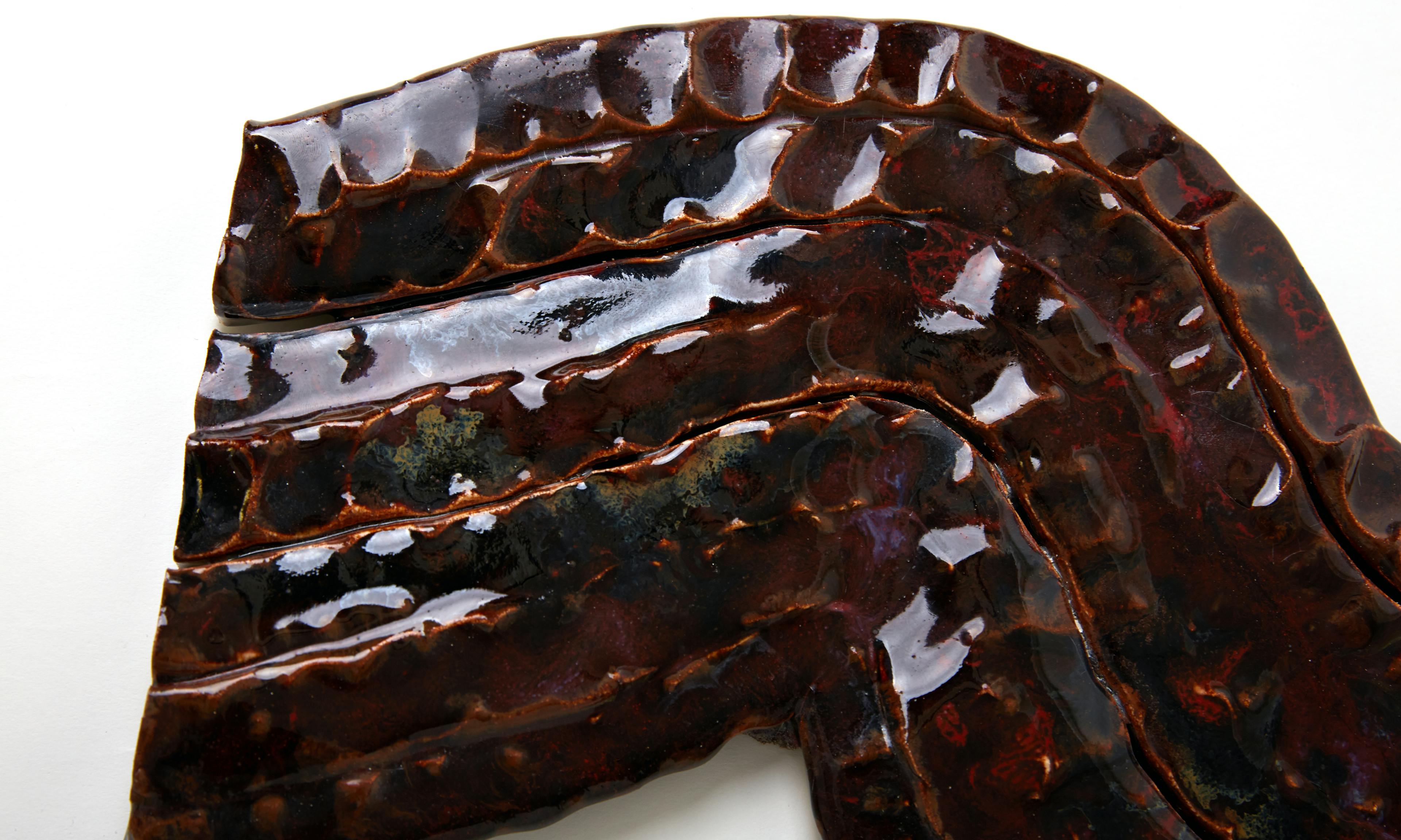 An image showing a zoom in of a glazes ceamic sculpture by Elena Gileva. It is shiny and maroon, purple. 
