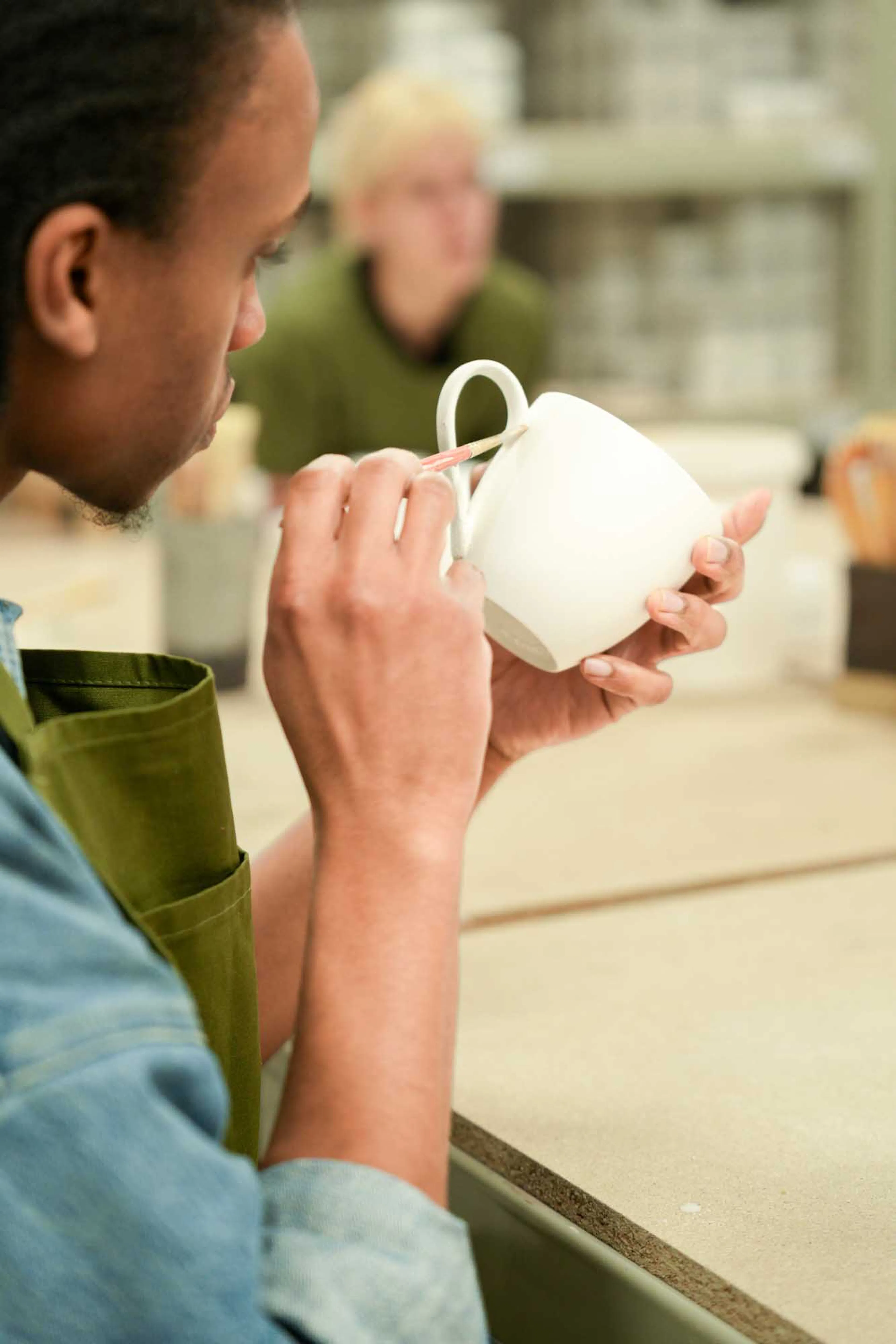 Paintipatiently painting pottery glaze onto  a stoneware mug with glaze