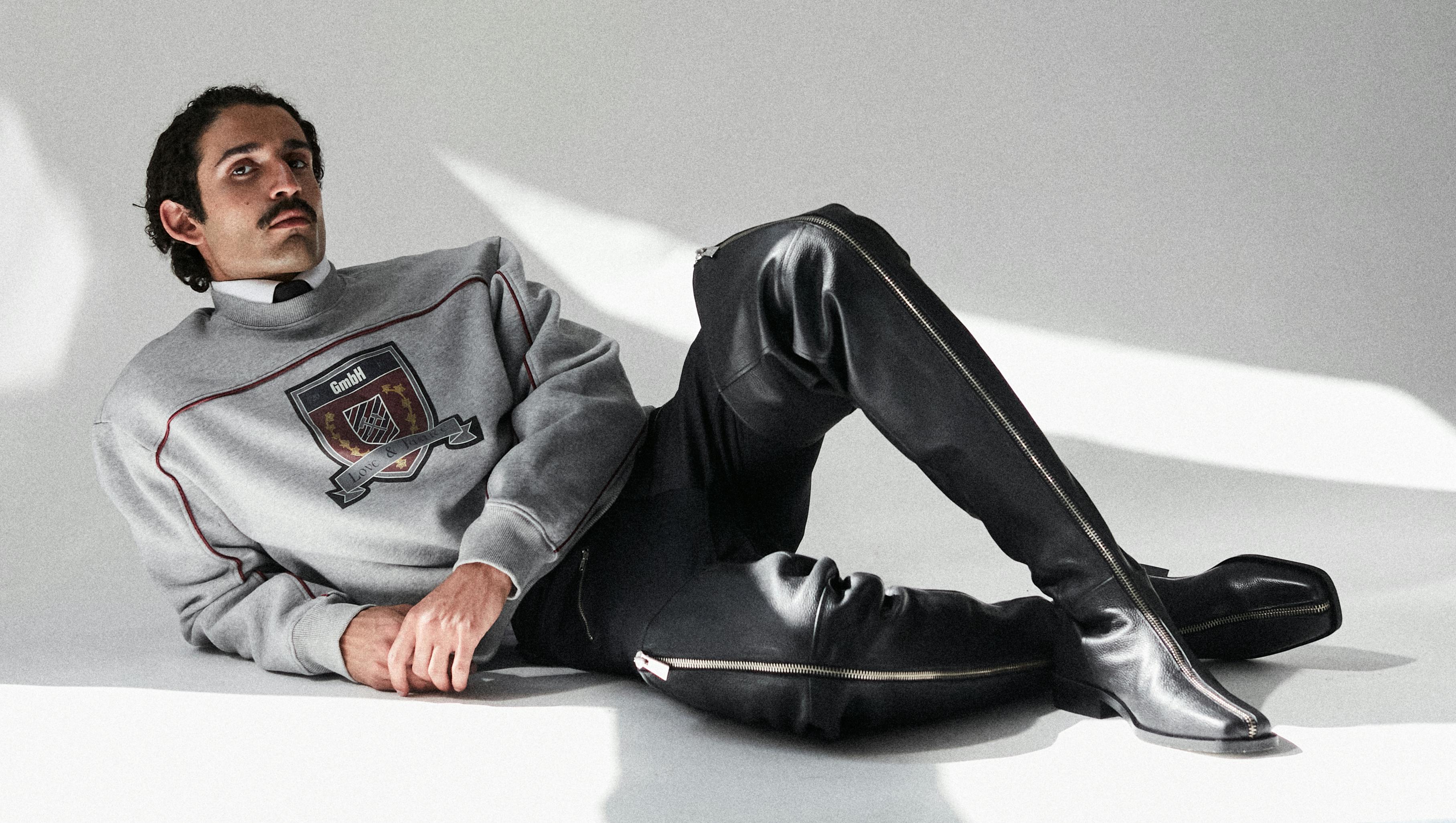 a handsome man is lying on the floor wearing a college sweater and thigh high boots