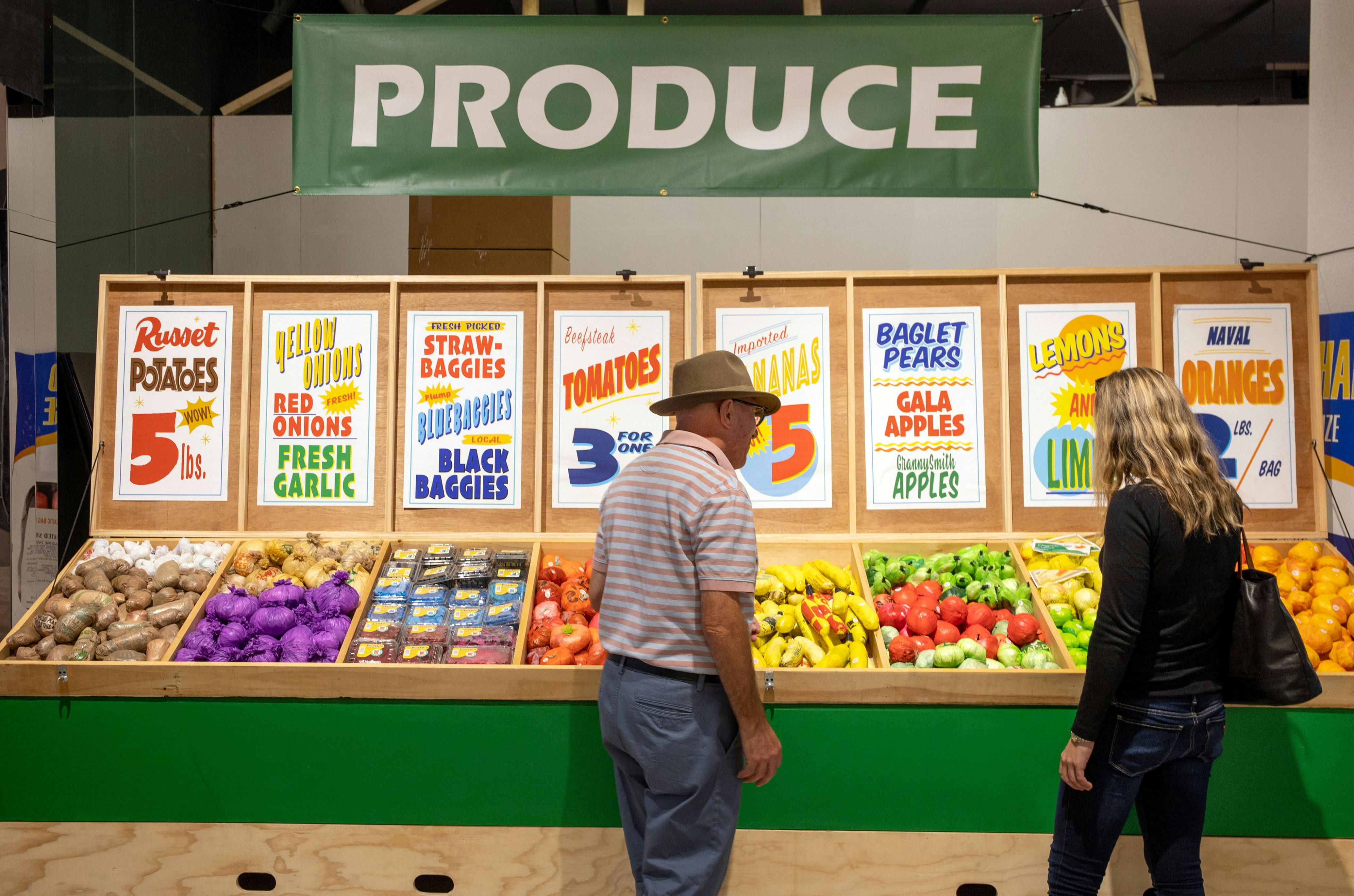 Two people stand in front of a fake produce stand at The Plastic Bag Store.