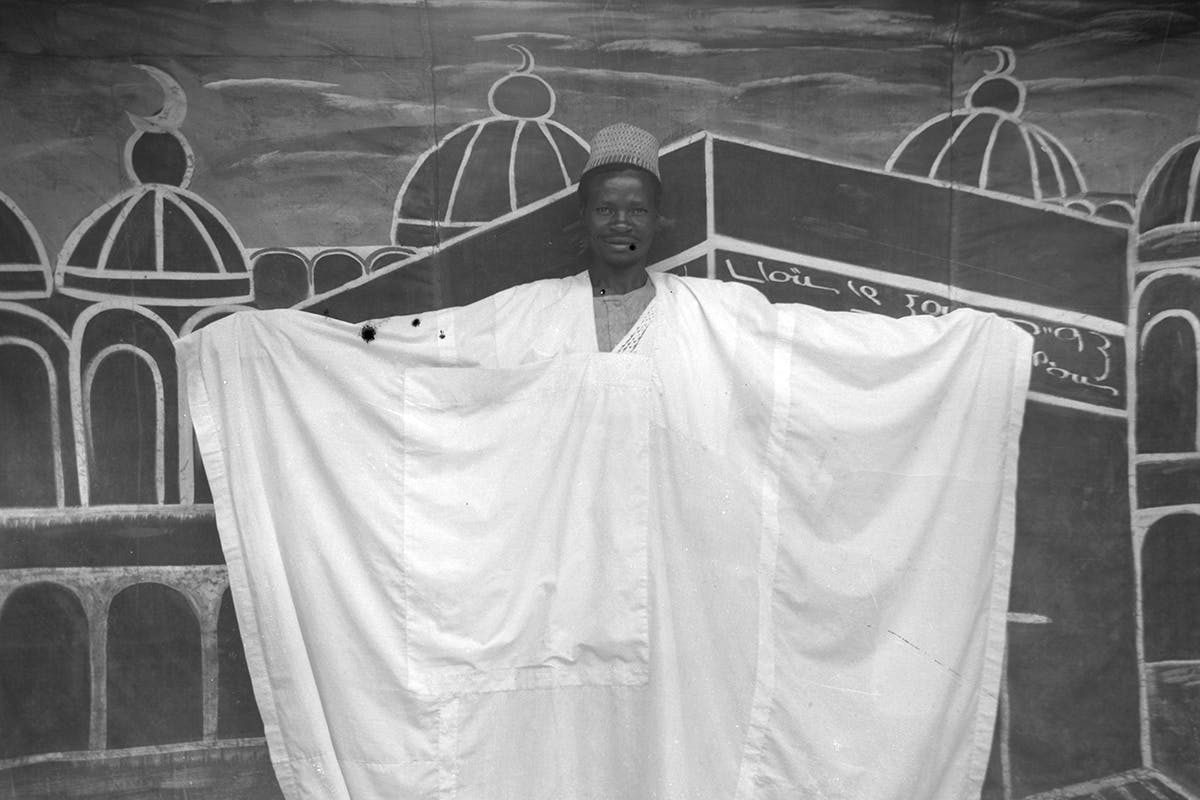 Black-and-white photograph of a man standing with his arms out, wearing a white robe in front of a hand-painted backdrop