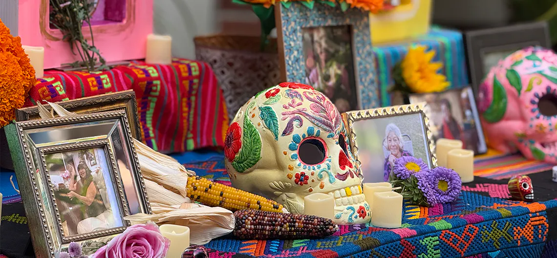 A table holds colorful fabrics, decorated ceramic skulls, flowers and photographs in ornate frames