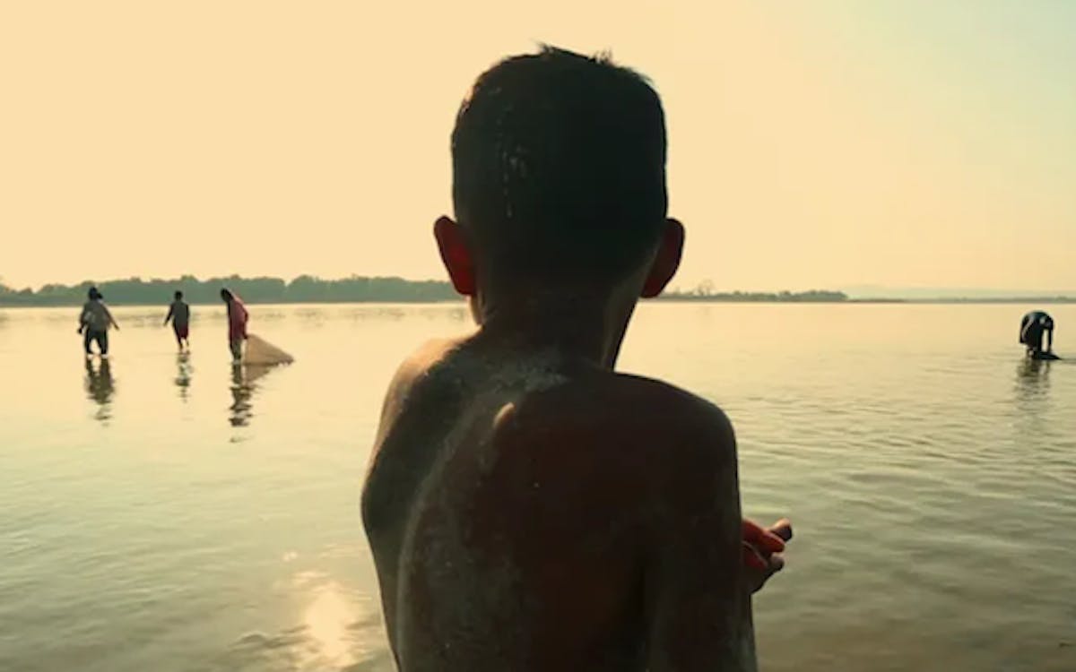 Seen from behind, a young boy watches a group of fisherman in a bay. Screenshot from the movie "Above and Below the Ground"