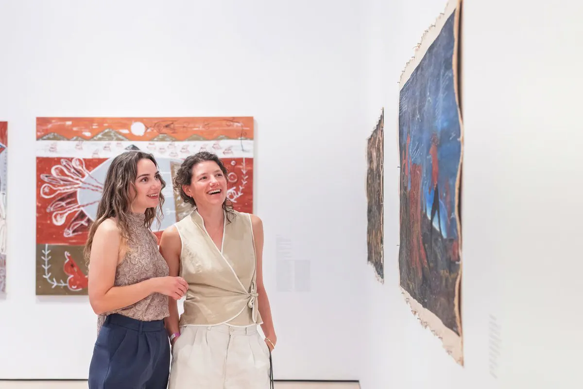 Two women look at a painting on a gallery wall together