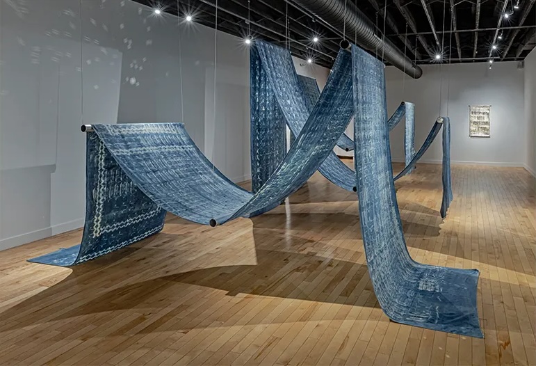 A gigantic blue tapestry hangs artfully draped from the ceiling in a gallery