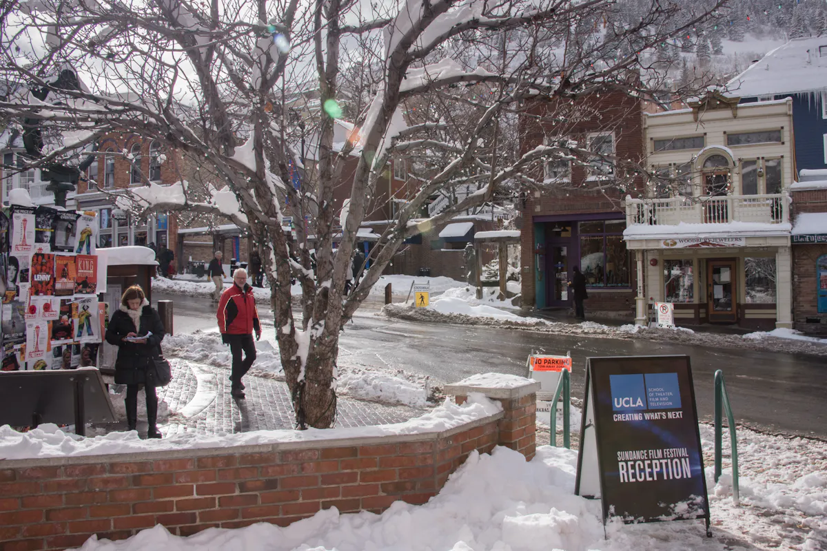 People walk down a snowy street. There is a sign in the foreground inviting people to a UCLA event