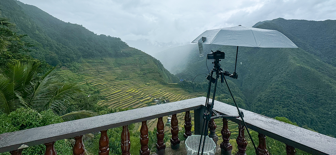 Image of a video camera set up pointing at a lush valley of rice farming