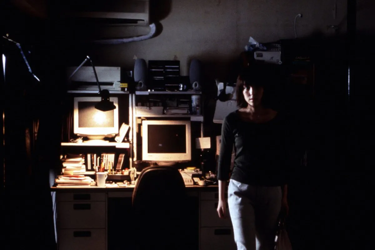 A woman standing in front of a computer desk in a dark room.