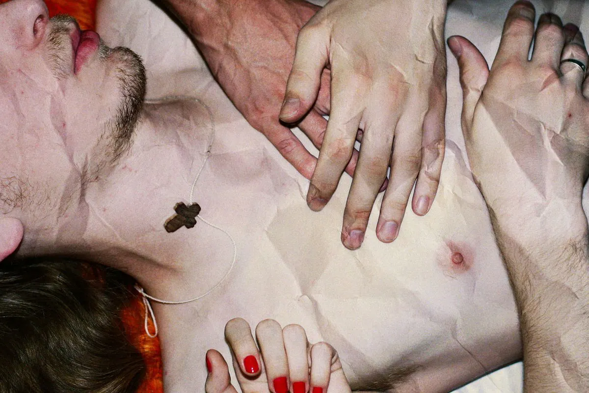 Crumpled image of a pale, topless man laying prone with two hands placed on their chest