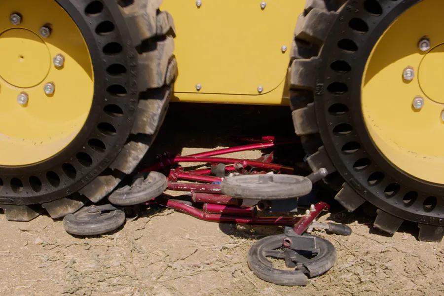 Image of truck wheels crushing a red wheelchair on a ground outdoor